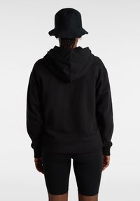 Zwarte hoodie met een relaxed fit, geribbelde manchetten en een kangoeroezak, gecombineerd met zwarte fietsbroekjes. Een bucket hat in dezelfde kleur.