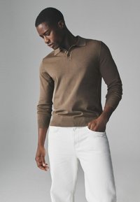 Brauner langärmeliger Poloshirt-Pullover aus glattem Strick, mit Kragen und gerippten Bündchen, kombiniert mit weißen geraden Hosen.