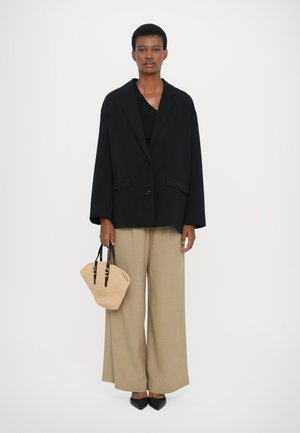 Blazer nera oversize sopra una maglia nera, pantaloni beige a gamba larga e una borsa intrecciata color tan con manici neri e scarpe nere a punta.
