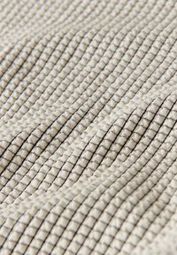 Texturiertem Stoff in hellem Beige mit subtilen schwarzen Streifen, der ein geripptes Muster aufweist, das Tiefe und visuelles Interesse schafft.