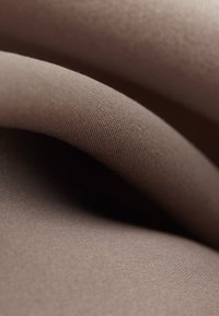 Gros plan d'un tissu marron doux et lisse avec des plis légers et une fine texture tissée, mettant en valeur son matériau et sa chute.