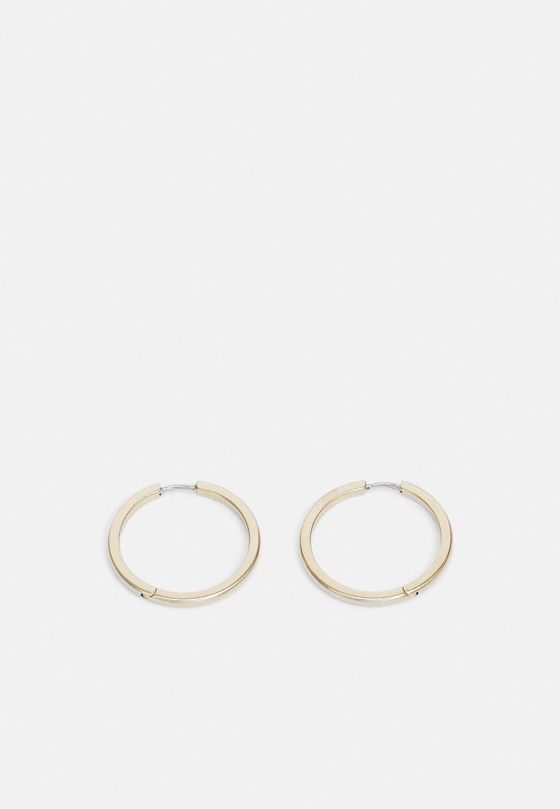 Paire de boucles d'oreilles créoles en or lisses de taille moyenne avec des fermoirs fins en argent sur un fond gris clair uni.
