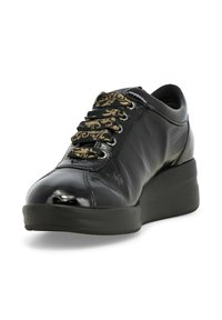 Scarpa in pelle nera con una finitura lucida, caratterizzata da occhielli decorativi a motivo dorato e una suola spessa e strutturata per un'altezza aggiuntiva.