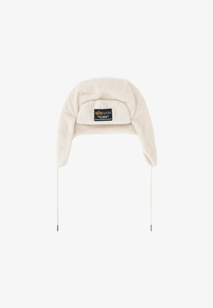 Cream-colored fleece trapper hat with ear flaps and a black rectangular label on the front reading Alpha Industries.