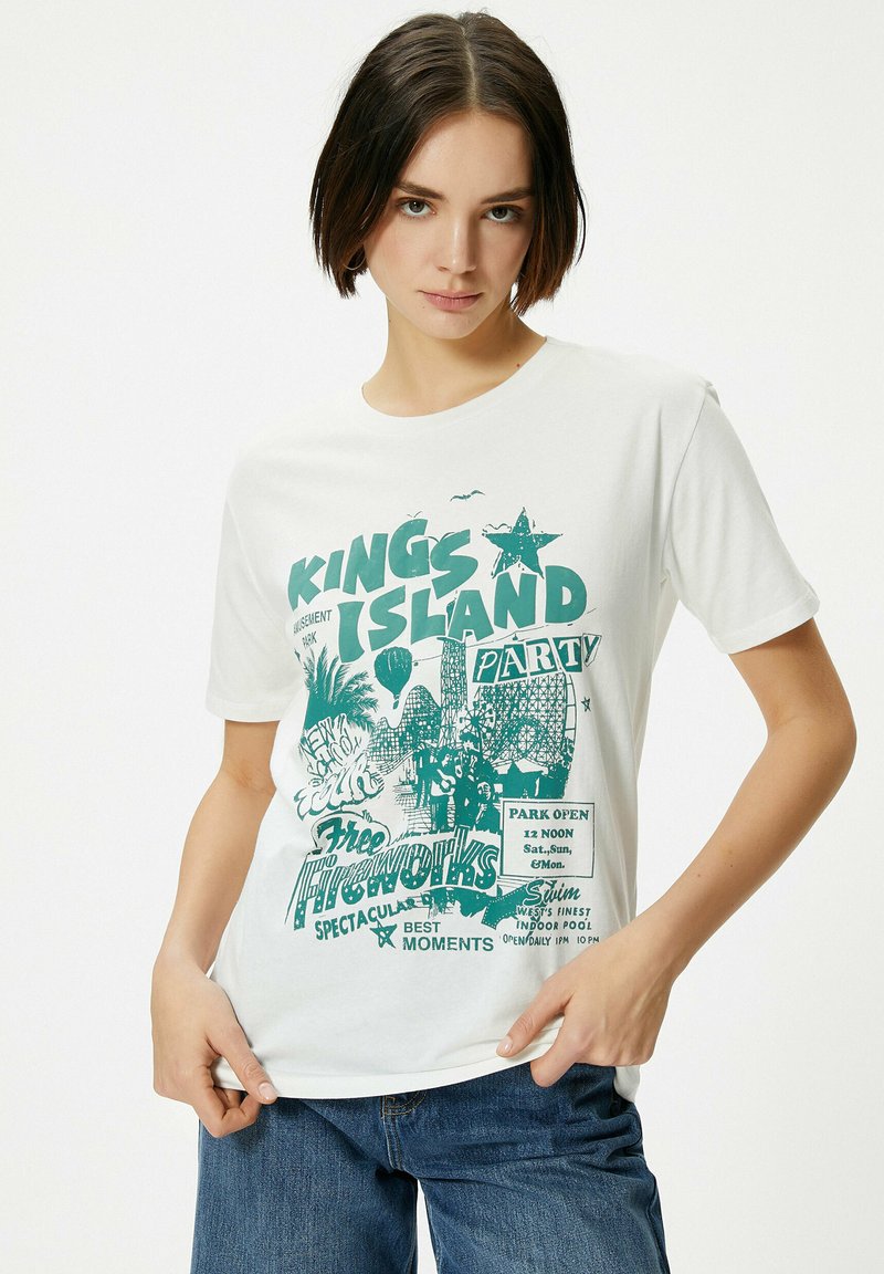 Hvid T-shirt med en turkis grafisk print og tekst om Kings Island forlystelsespark, der viser en stjerne, palmetræer og forlystelser.