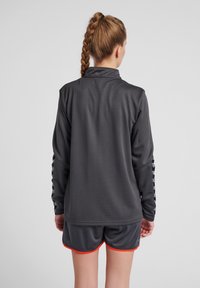 Donkergrijze sportieve long-sleeve top van textuurstof, met een kraag en zwarte strepenaccenten langs de mouwen, gecombineerd met donkere shorts.