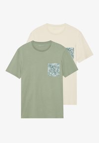 Two t-shirts: one in olive green with a floral-patterned pocket, and one in cream with a matching floral pocket. Short sleeves, round neck.