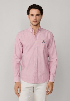Camisa de botón a rayas rojas y blancas con cuello, mangas largas y logo bordado en el lado izquierdo del pecho. Tejido de algodón con textura suave.
