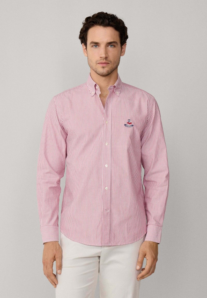 Camisa de botón a rayas rojas y blancas con cuello, mangas largas y logo bordado en el lado izquierdo del pecho. Tejido de algodón con textura suave.