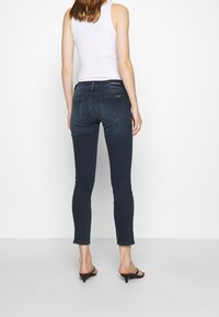 Jeans skinny in denim scuro con vita media, dotati di tasche posteriori e dettagli di cucitura minimi, abbinati a sandali neri con tacco.