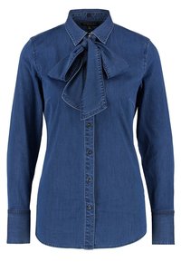 Denimskjorta i mörkblått med knapplist framtill, spetsig krage och stor fluga vid halsen. Långa ärmar med knäppningar vid handledarna.