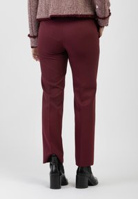 Pantaloni slim-fit borgogna con una texture liscia, caratterizzati da una leggera apertura alle caviglie, abbinati a stivali neri con tacco.