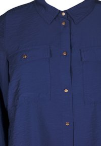 Camicia blu navy con una texture stropicciata, dotata di colletto a punta, bottoni frontali e due tasche a pattina con bottoni a pressione in tono oro.