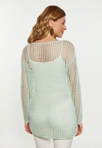 Maglione a maniche lunghe di un verde menta chiaro, lavorato a maglia con un grande design a trama aperta. Presenta un ampio scollatura e un orlo posteriore leggermente più lungo.