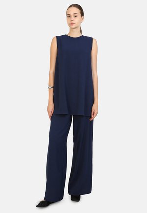 Top sin mangas de color azul marino con escote redondo, combinado con pantalones de pierna ancha, ambos hechos de una tela suave y texturizada. Diseño simple, acentos mínimos.