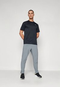 Svart atletisk t-shirt med korta ärmar och texturerad design, kombinerad med ljusgrå avsmalnande joggers och svarta sneakers. Enkel, funktionell stil.