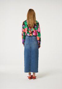 Jeansmaxi rok met knoopdetails aan de zijkant, gecombineerd met een kleurrijke bloemenblouse. De blouse heeft groene, roze en paarse tinten op een donkere achtergrond.
