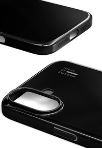 Svart mobildeksel med blank overflate. Har utskjæring for kamera, tilgang til knapper, og "IDEAL OF SWEDEN" merkevare. Myk tekstur, elegant design.