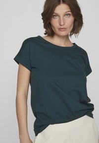 Dark teal short-sleeve t-shirt with a round neckline. Made of soft fabric, featuring a relaxed fit and rolled-up sleeve cuffs.
