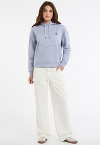 Felpa azzurra chiara con tasca frontale e cordini, abbinata a pantaloni cargo larghi color crema con tasche laterali e vestibilità rilassata.