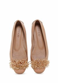 Bailarinas de cuero beige con plantilla texturizada y un adorno floral de cuentas en la punta. Forma suave y redondeada, diseño clásico.