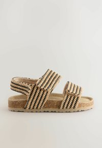 Vävd beige och svart sandal med remmar, justerbara kardborrelås och texturerad korkfotbädd; platt sula med räfflade kanter.
