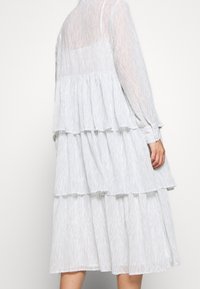 Vestido azul claro de capas hecho de tela transparente, con sutiles patrones de ondas, mangas largas y una silueta fluida.