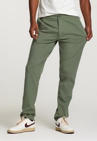 Pantaloni verzi dintr-un amestec de bumbac cu o croială relaxată, având închidere cu nasture și buzunare laterale, asortați cu adidași albi și bordo.