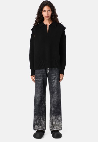 Schwarzer übergroßer Pullover mit Kragen, ausgestattet mit gerippten Bündchen und Ärmeln. Kombiniert mit weit geschnittenen, verwaschenen schwarzen Jeans und schwarzen Clogs.