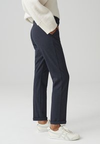 Pantaloni navy su misura con taglio dritto, dotati di tasche frontali e risvolti, abbinati a sneaker bianche sportive.