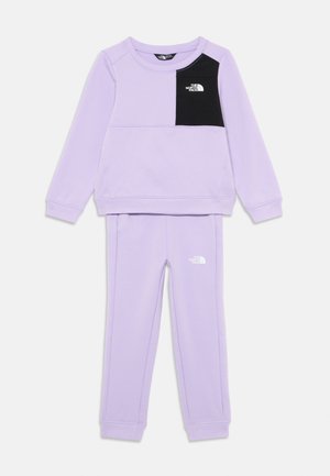 L'ensemble en lilas comprend un sweatshirt à col rond avec une poche noire sur la poitrine et un logo, associé à un pantalon de jogging assorti avec le logo sur la jambe.