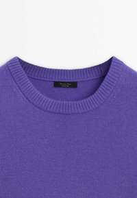 Pull en maille violet avec col rond côtelé et étiquette de marque noire cousue à l'intérieur du col.
