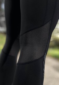 Leggings noirs avec un panneau en maille texturée au niveau du genou, tissu lisse et rayures latérales contrastantes pour un détail de design.