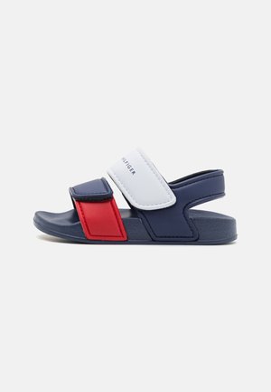 Sandale enfant à bout ouvert avec semelle bleu marine, bride avant rouge, bride centrale blanche avec texte de la marque, et bride de cheville bleu marine avec fermeture Velcro.