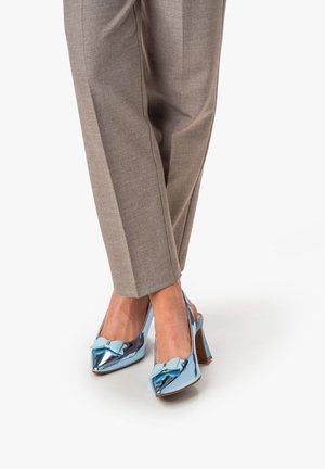 Zapatos de tacón alto tipo slingback en un brillante cuero sintético azul claro, con puntera puntiaguda y un lazo menta como acento, combinados con pantalones grises claros de corte ajustado.