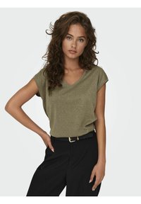 Top de color verde oliva, de manga corta y corte holgado, con cuello en V, hecho de una tela texturizada con un ligero brillo, combinado con pantalones negros de talle alto.