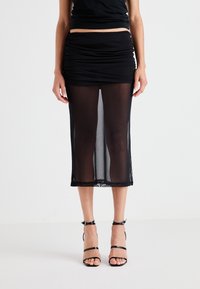 Schwarze Midirock mit gerafftem Design, transparenter Stoff und Spitzenrand am Saum. Kombiniert mit schwarzen Riemchen-Absätzen.