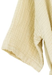 Smėlio spalvos tekstūruota medžiaga su raukšlėtu raštu, plačiomis rankovėmis ir banguota apačia. Lengva ir orui pralaidi medžiaga.