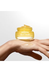 Tydlig glasburk med en gul fuktgivande mask med en slät, geléliknande konsistens, vilande på en hand. Etiketten innehåller varumärkesnamn och produktinformation.