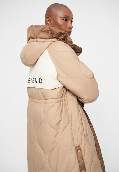 Vatteret beige pufferjakke med en brun hætte og hvid panel bagpå, der har "WEEKEND" i sort tekst. Har snaplukninger og sidelommer.