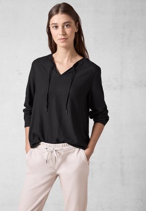 Zwarte lange mouw top met een V-hals en trekkoorden, met een gestructureerd oppervlak. Gecombineerd met lichtbeige, elastische broeken met een tailleband.