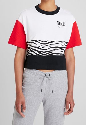 Woman wearing a cropped Nike t-shirt with red sleeves, white top and black-and-white zebra print stripe, paired with grey sweatpants.