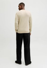Beige gebreide trui met geribbelde manchetten en zoom, gecombineerd met losse zwarte broek en zwarte schoenen, toont een gladde textuur en een eenvoudig ontwerp.
