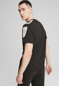 Mustapaita, jossa on vihreät ja valkoiset korostukset olkapäillä, pyöreä kaula-aukko, pehmeä materiaali ja rento istuvuus.