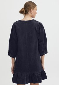 Marine-blaues Corduroykleid mit 3/4-Puffärmeln, Rückenzipper und rüschengesäumtem Saum, das ein strukturiertes geripptes Muster aufweist.