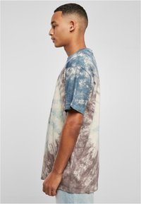 T-Shirt mit kurzen Ärmeln im Batikdesign, das wirbelnde blau-, beige- und brauntöne zeigt. Der Stoff wirkt weich und hat eine lockere Passform sowie einen Rundhalsausschnitt.