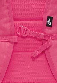 Φωτεινό ροζ υλικό σακιδίου με υφή, διαθέτοντας πλαστικό κλιπ και ρυθμιζόμενους ιμάντες. Ετικέτα λογότυπου Nike στο πλάι.