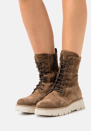 Brown suede lace-up ankle boots with side zipper and white thick ridged soles worn on bare legs.