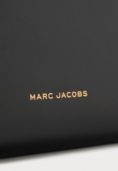 Surface noire avec texte doré en majuscules Marc Jacobs centré dessus.