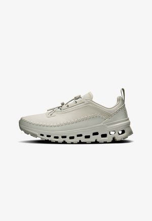Hellgrauer Sportschuh mit einem glatten Textiloberteil, strukturierten Nahtdetails und einer gepolsterten Sohle mit Belüftungslöchern.